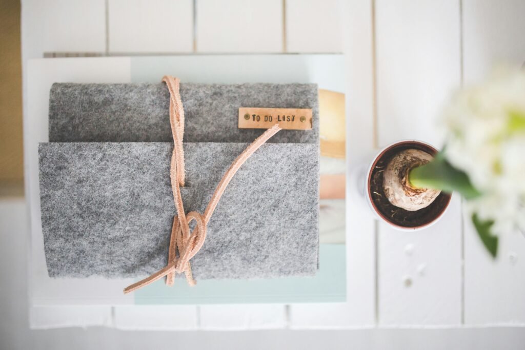 Flat lay of a gray felt notebook with a to-do list tag and a small potted plant on a white desk.